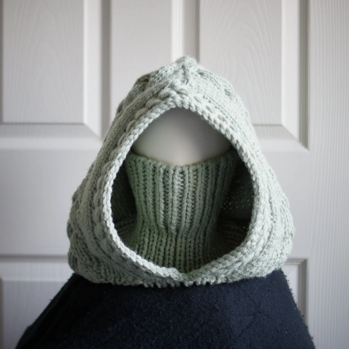 Sage green knit balaclava worn by mannequin, side view with turtleneck rolled up to cover face