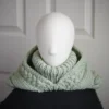 Sage green knit balaclava worn by mannequin with hood dropped down