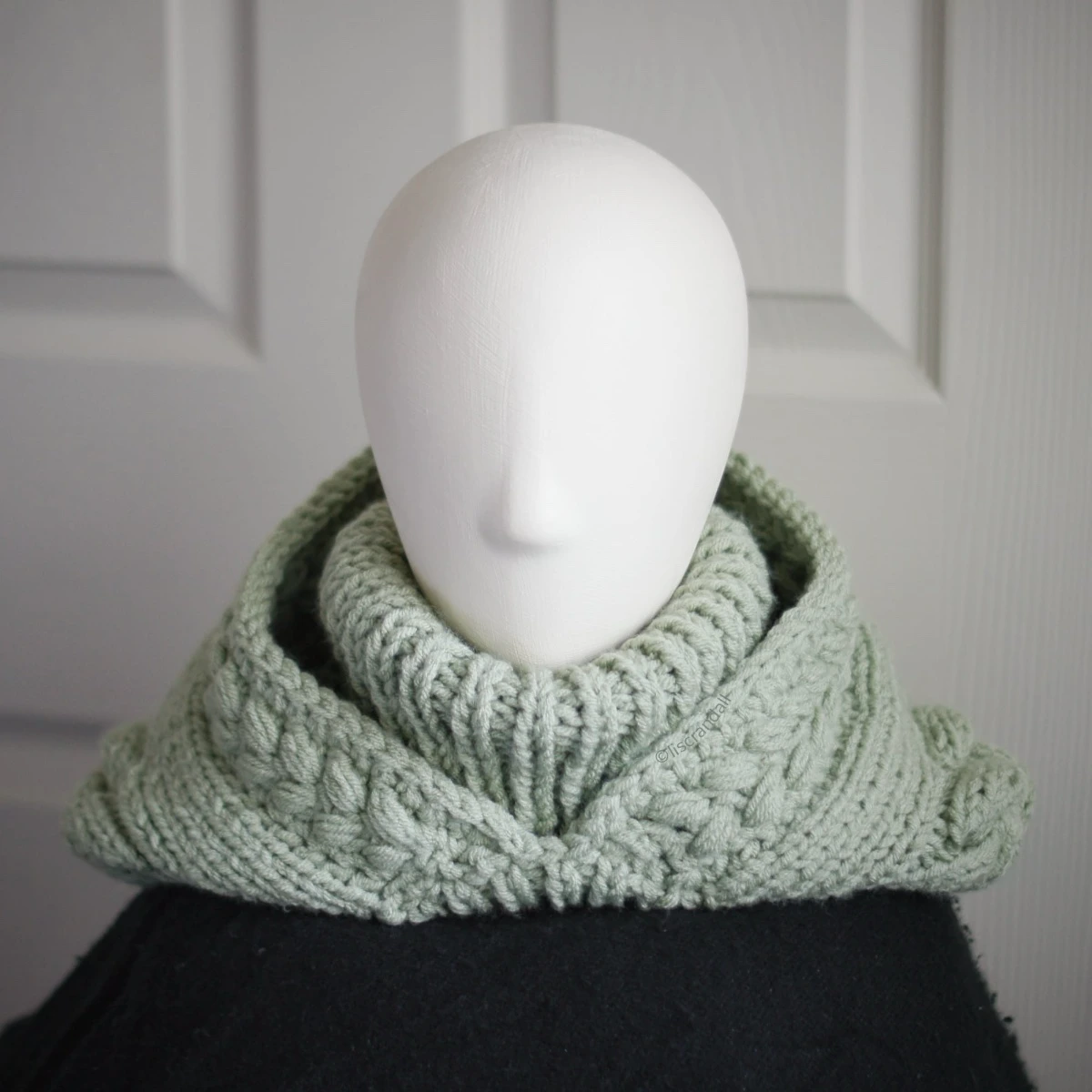 Sage green knit balaclava worn by mannequin with hood dropped down