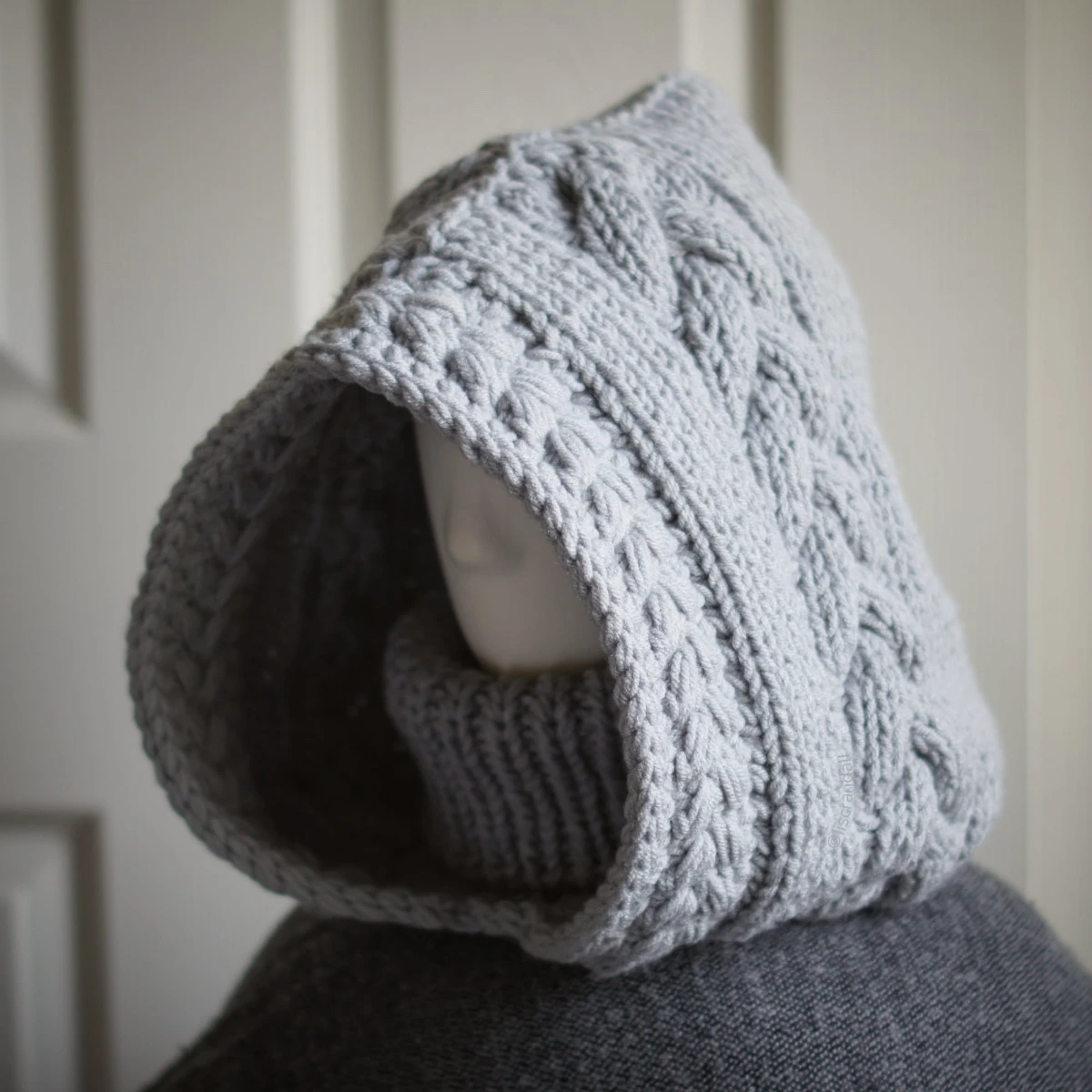 Handmade knit balaclava in light grey with cable details and wheat stitch edging, side view showing cable details
