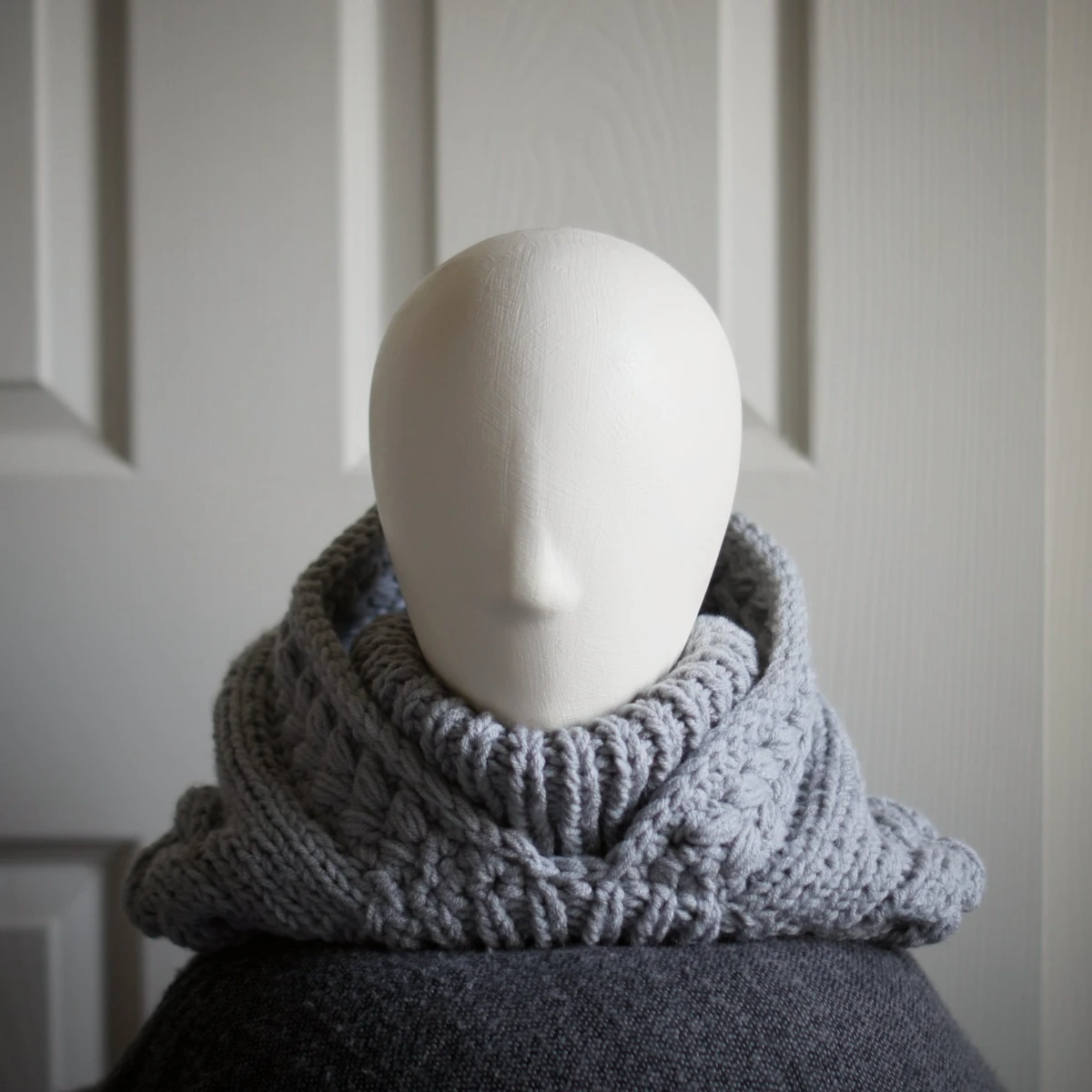 Handmade knitted balaclava in light grey with cable details and wheat stitch edging, front view with hood dropped back