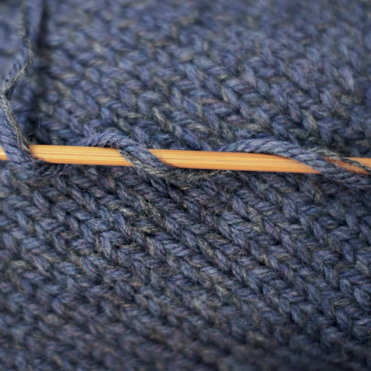 Denim blue merino wool with a strand of cashmere wool on bamboo knitting needle over knitted fabric