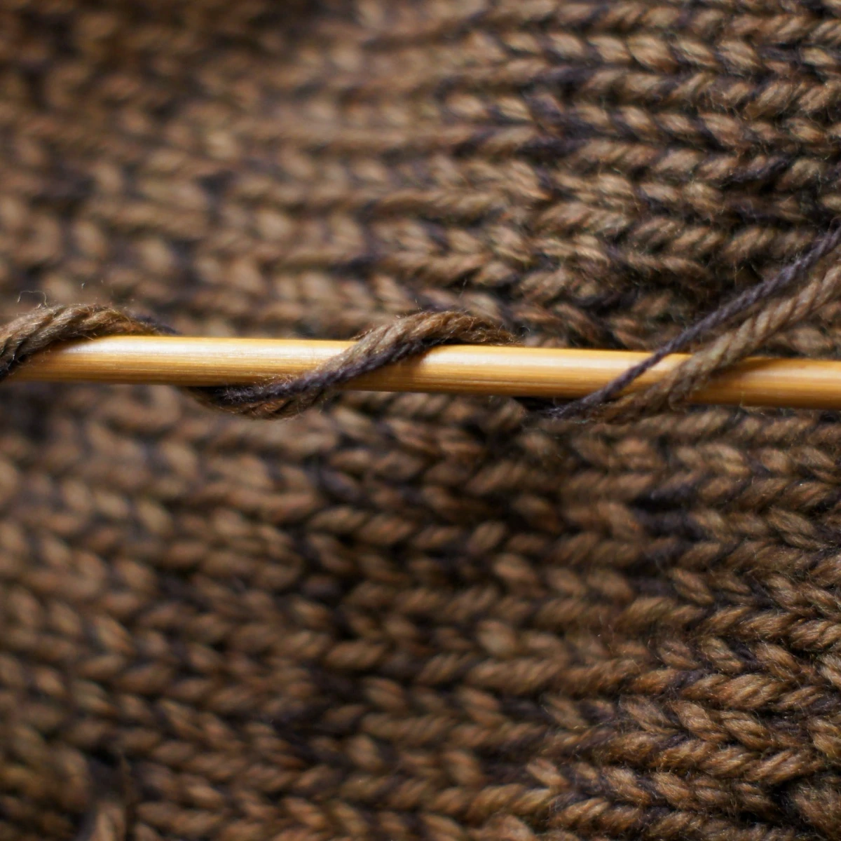 Coffee merino wool with a strand of cashmere wool on bamboo knitting needle over knitted fabric