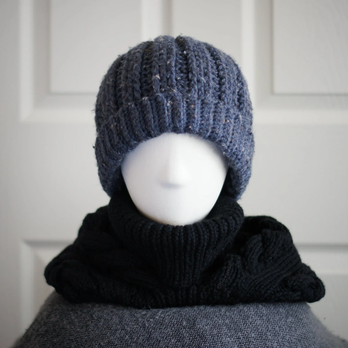 Black merino knit balaclava hood with twist edging and folded turtleneck worn by mannequin, hood dropped down