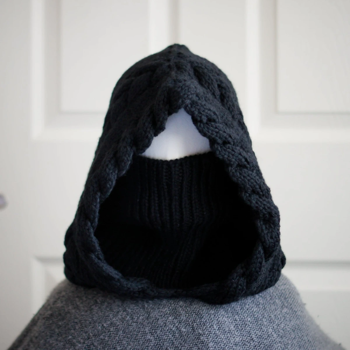 Black merino knit balaclava hood with twist edging and folded turtleneck worn by mannequin, styled with turtleneck rolled up to cover face